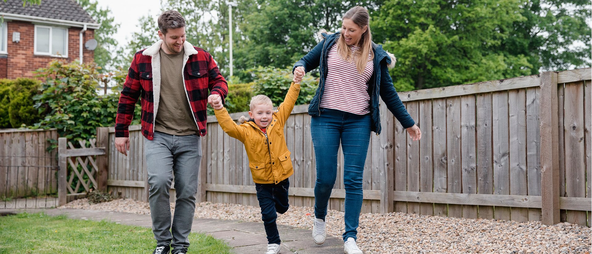 Das Foto zeigt eine fröhliche Situation einer Familie, bestehend aus Vater, Mutter und Kind, in einem Garten